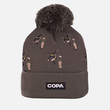 Brown COPA beanie with embroidered bicycle kick footballers pattern, pom-pom on top, and COPA logo patch on the cuff