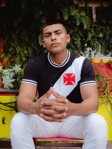 Person wearing a black and white Vasco da Gama shirt with a red logo, sitting outdoors.