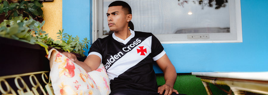 Person wearing a black and white Vasco da Gama Shirt with visible branding, sitting on a bench.