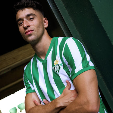 Model wearing the Real Betis 1976 - 77 Retro Football Shirt, posing against a wooden background.