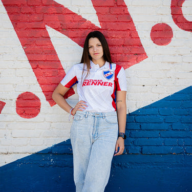 Woman wearing a retro Nacional football shirt with Pinturas Renner sponsor, standing in front of a red, white, and blue mural.