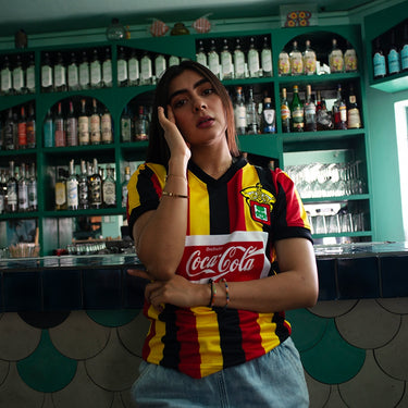 Leones Negros udeG 1992 - 93 Retro Football Shirt Yellow, Red & Black Lifestyle worn by a model in a bar setting.