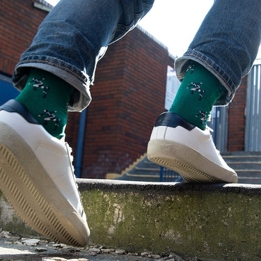 model wearing casual green socks with a repeating pixel-style illustration of eric cantona football moment kung fu