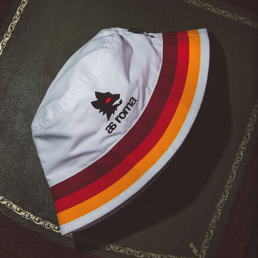AS Roma bucket hat placed on a dark surface, showing its embroidered logo and stripe details
