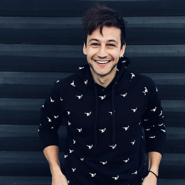 Model smiling while wearing the Panini Hooded Sweater in front of a striped wall.