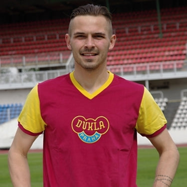 Model wearing the Dukla Prague 1960's Retro Football Shirt, posing in a stadium.