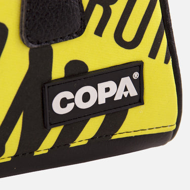 Close-up of COPA logo stitched on yellow recycled fabric with black zipper edge.